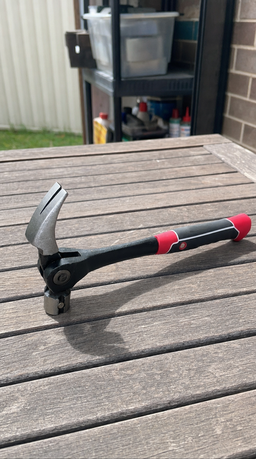 The claw hammer with its red and black grip resting on a wooden outdoor table