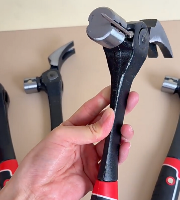 A hand holding the claw hammer upright with a nail resting in the magnetic slot of the head