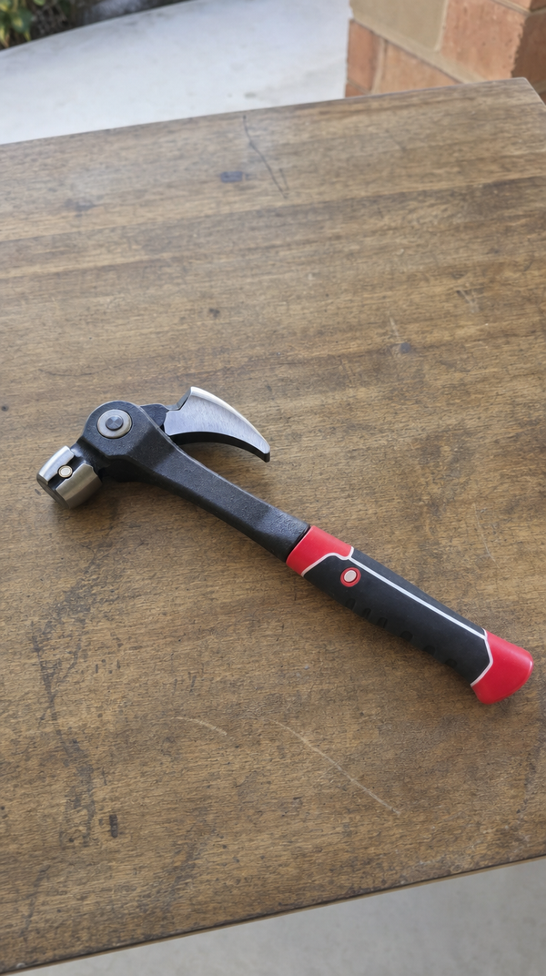 The claw hammer with a red and black grip lying on a wooden table