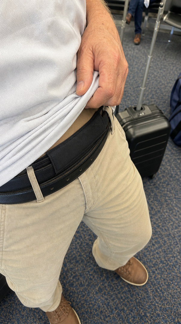 Hidden money belt pouch worn behind a belt, shown with a shirt lifted at the airport